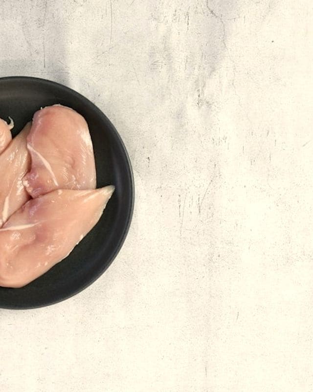 Два сырых куриных филе на тёмной тарелке